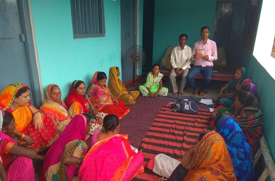 गांव में दरी पर बैठी महिलाओं की बैठक में संगठन के पदाधिकारी बात करते हुए