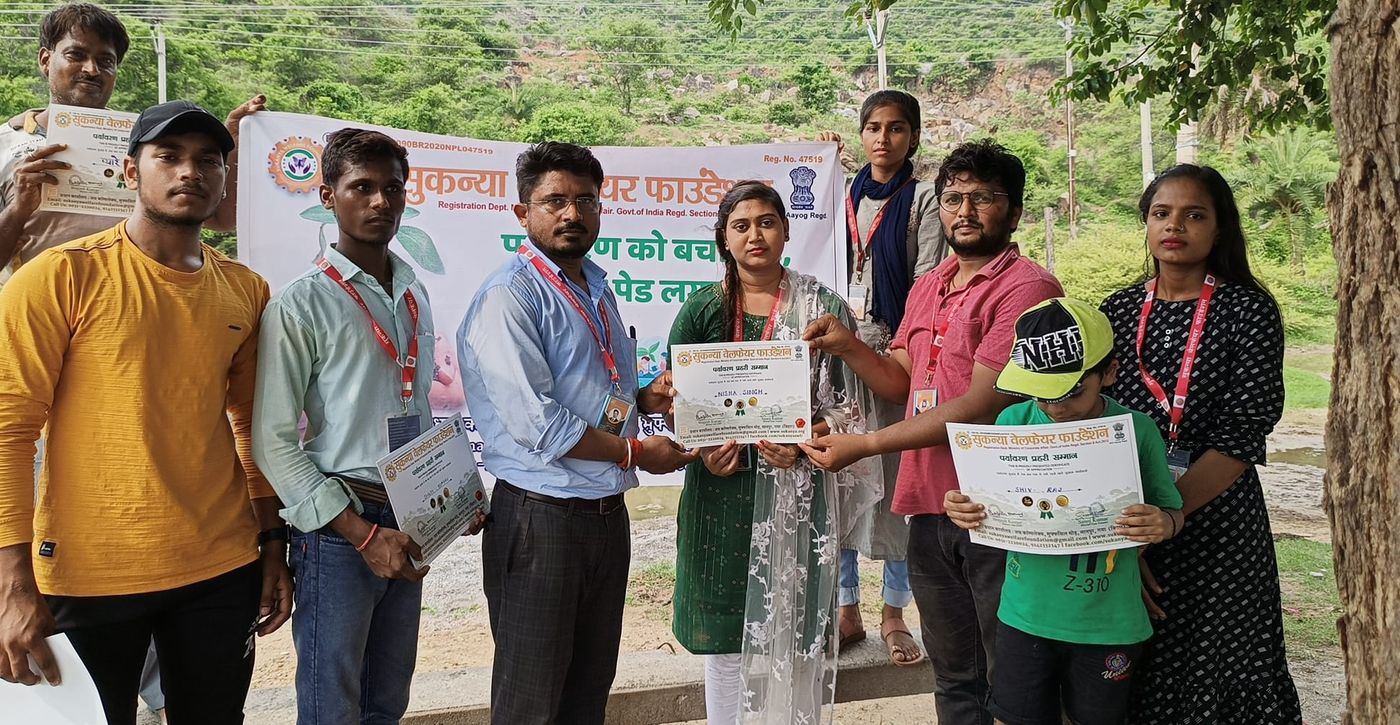 पर्यावरण अभियान के बैनर के सामने प्रमाण पत्र लिए युवा